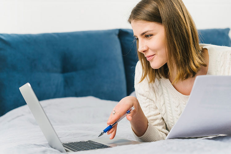 Happy woman holding papers & pen working on laptop on the couch